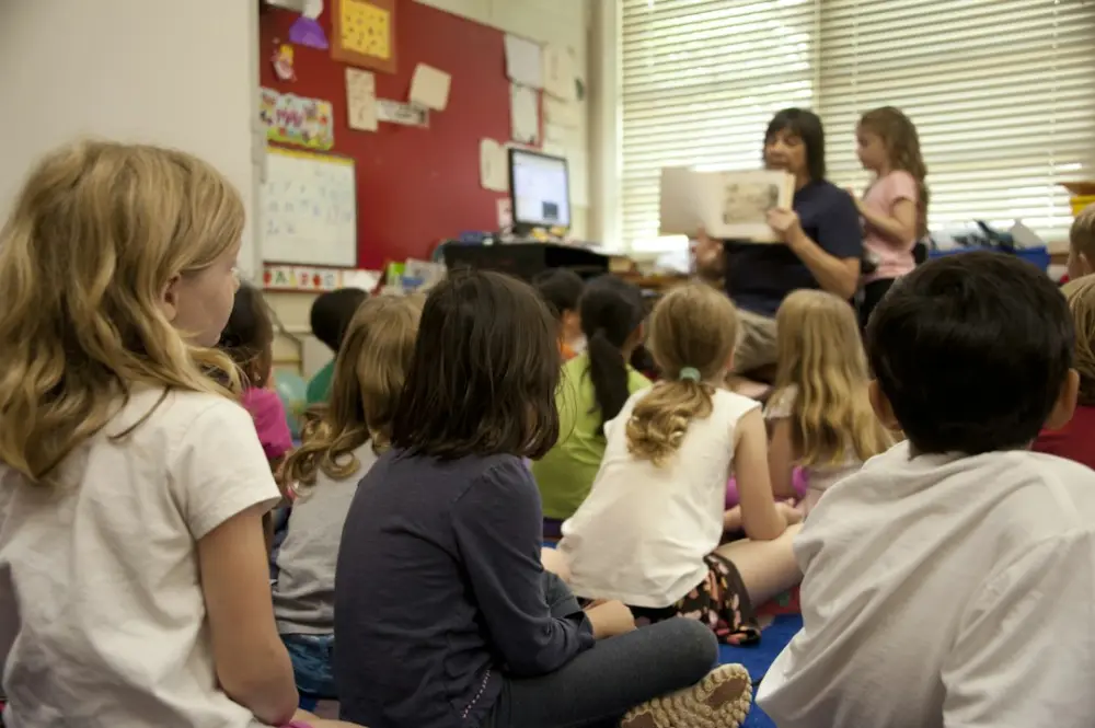 A group of children sitting on a classroom floor listening to a story, illustrating classroom adaptations for developmental